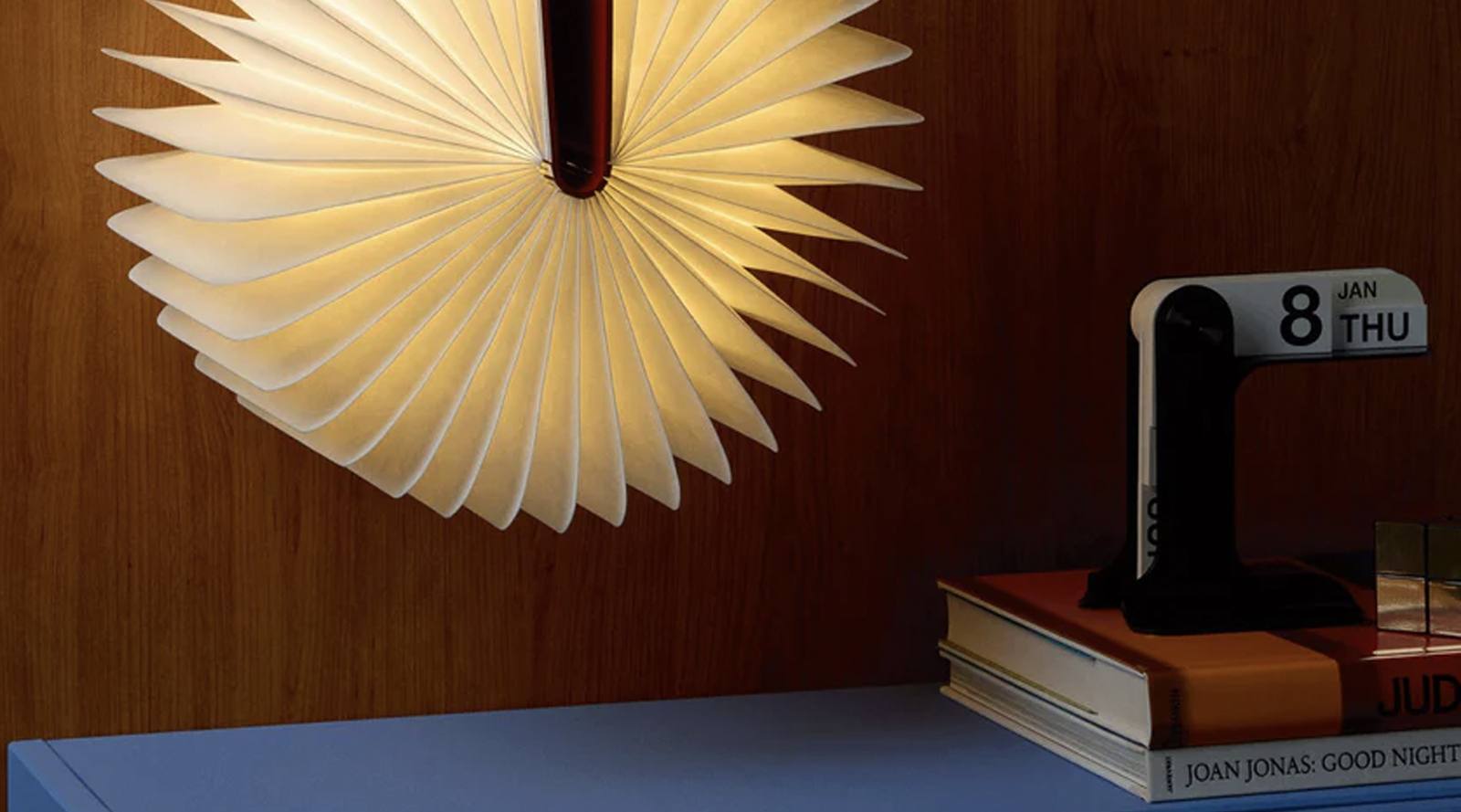 A sculptural folded-paper light mounted against a warm wood-paneled wall
